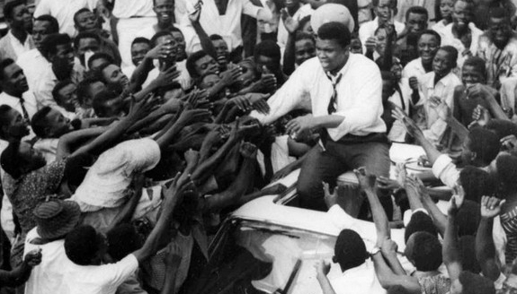Muhammad Ali in Nigeria sitting on top of a car greeting a huge crowd of people in 1964.