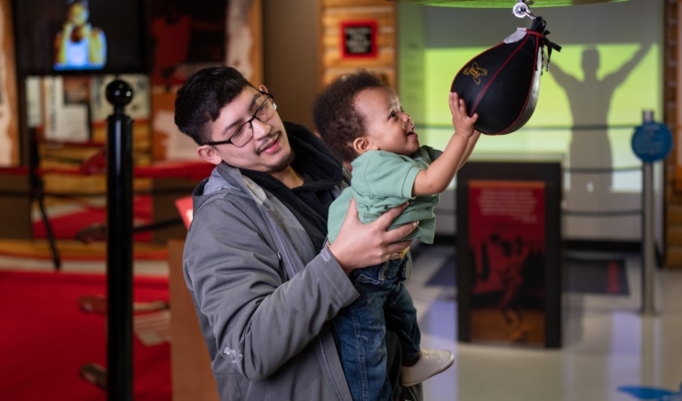 Father and toddler child in the Deer Lake exhibit playing with a speed bag