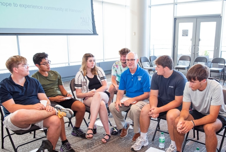 A man with a blue Hanover College polo seated with a group of students