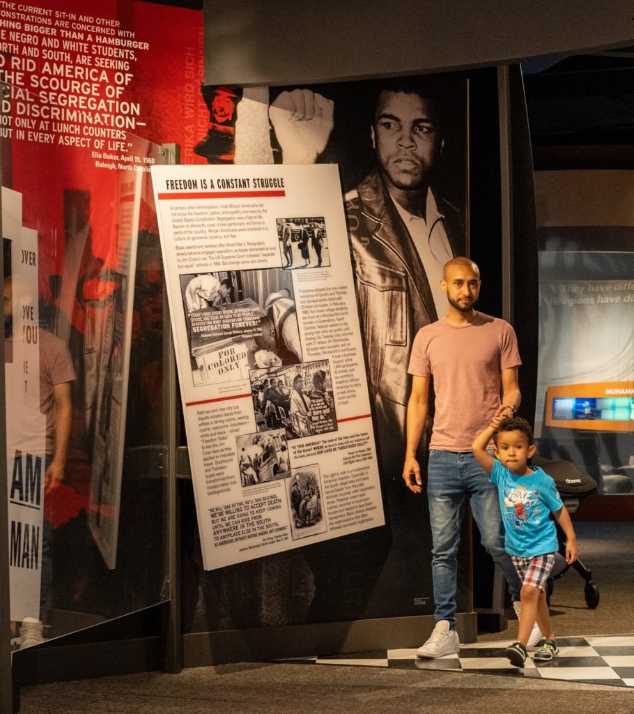 Father and young son walking through exhibit gallery full of text panels