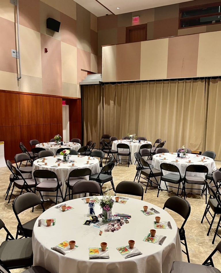 Room with large round banquet tables and folding chairs set up for an event