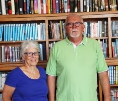 Woman wearing blue blouse and man wearing green polo shirt posing in front of library bookshelf