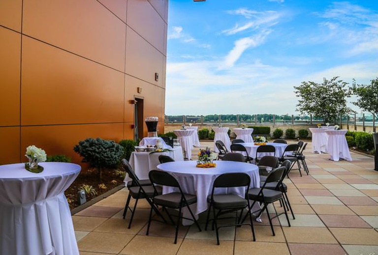 Round banquet tables and folding chairs set up for an event on a patio