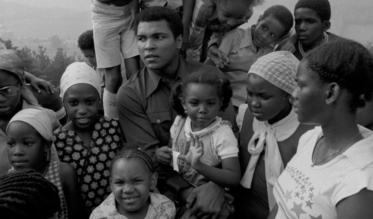 Black and white photo of Muhammad Ali outside with a large group of children