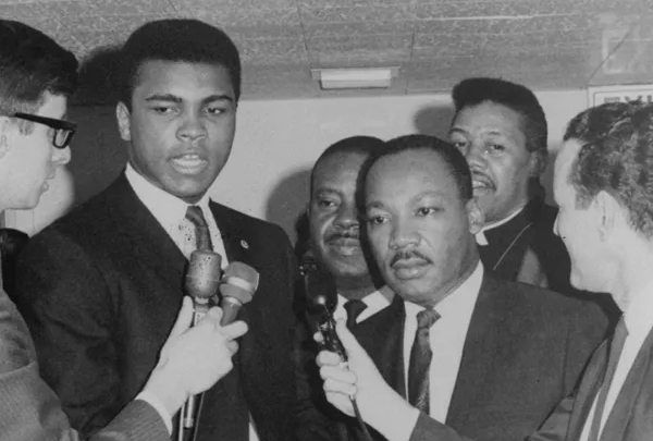 Black and white photo of Muhammad Ali and Martin Luther King Jr. in suits being interviewed