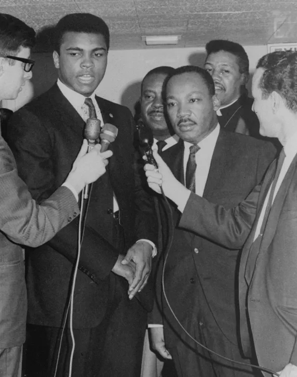 Black and white photo of Muhammad Ali and Martin Luther King Jr. in suits being interviewed