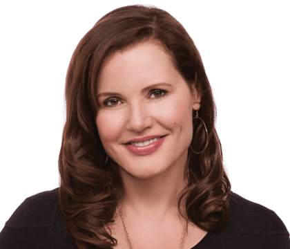 Geena Davis, wearing black top and gold necklace, smiles at camera