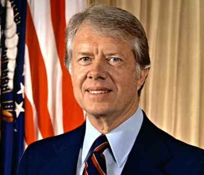 Jimmy Carter, wearing dark blue jacket, blue shirt and red and blue tie posing for camera