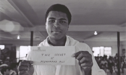 Muhammad Ali in a robe holding a white envelope with the words "The Secret of Muhammad Ali" handwritten on it