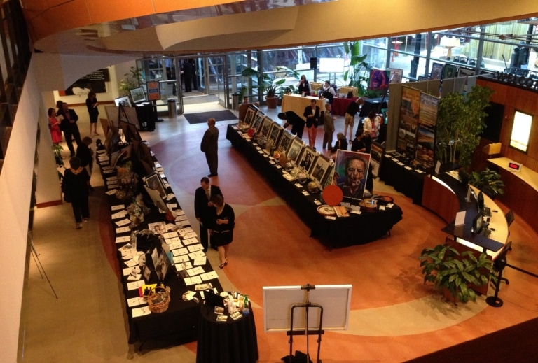 A large room with rows of tables of artwork and other things for sale or action while people in business attire review the items