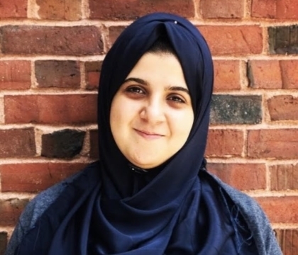 Woman wearing dark blue hijab and blue shirt posing in front of brick wall