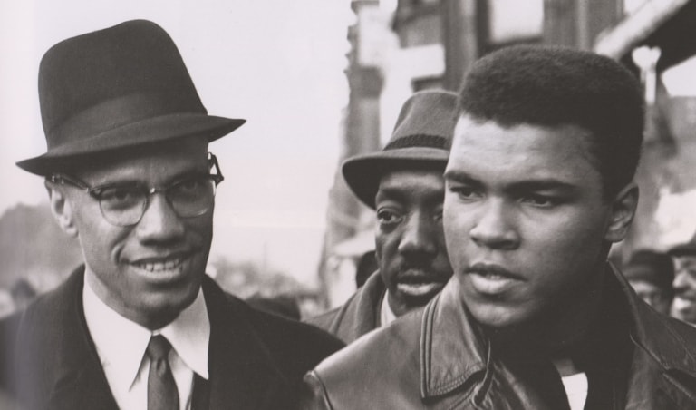 Black and white photo of Muhammad Ali and Malcolm X as young men walking on the street
