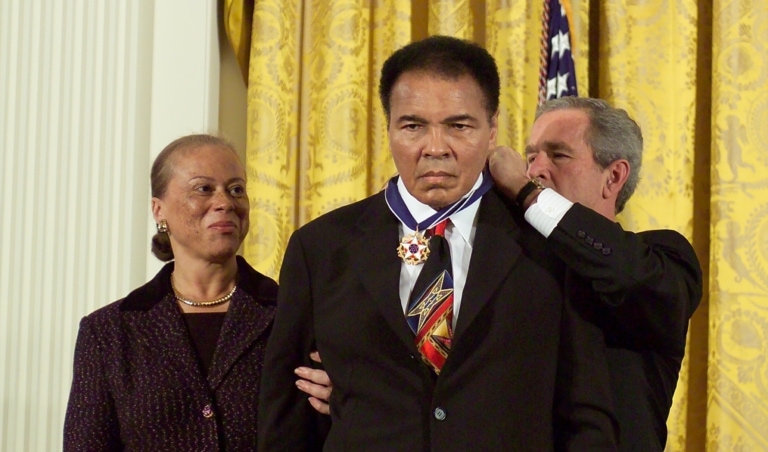 Muhammad Ali in a suit receiving the Medal of Freedom from President George W. Bush