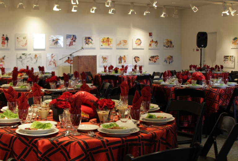 Art gallery set up for an event with large banquet rounds, red tablecloths, and black folding chairs