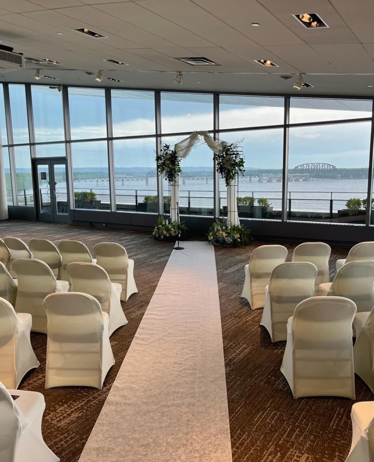 A wedding ceremony set up in a large room with large windows.