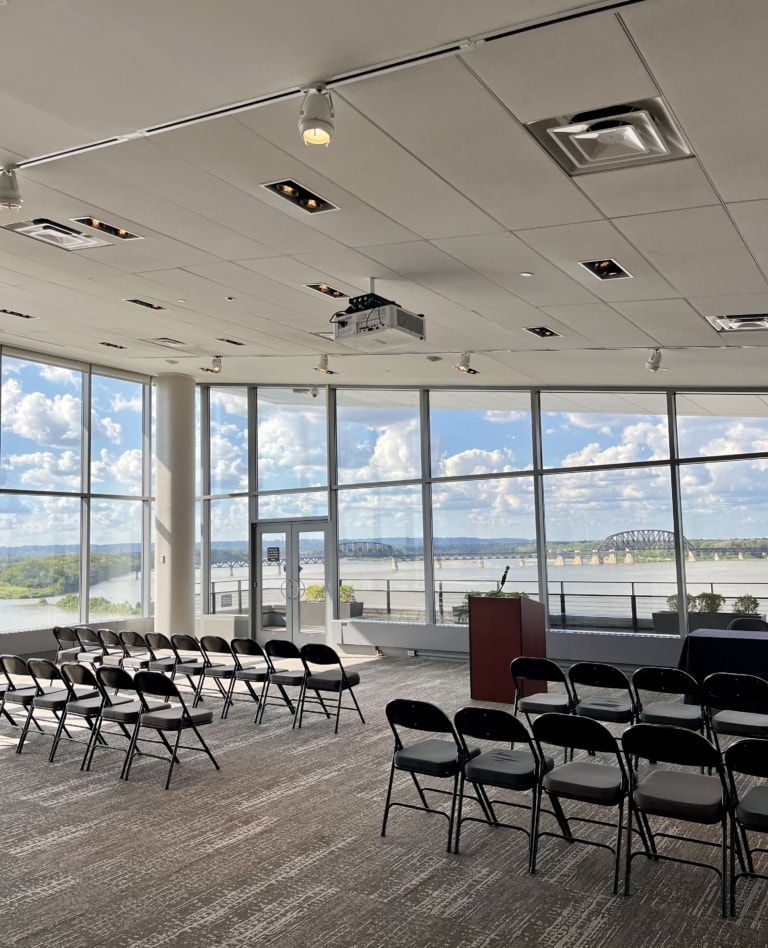 A lecture set up in a large room with large windows.