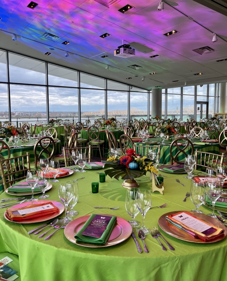 A large room of windows filled with colorful place settings on green banquet tables
