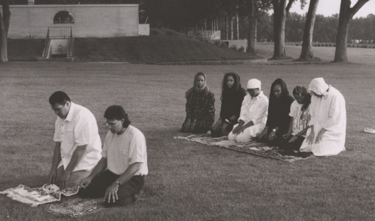 Black and white photo of Muhammad Ali kneeling on the grass and praying with his family and guests