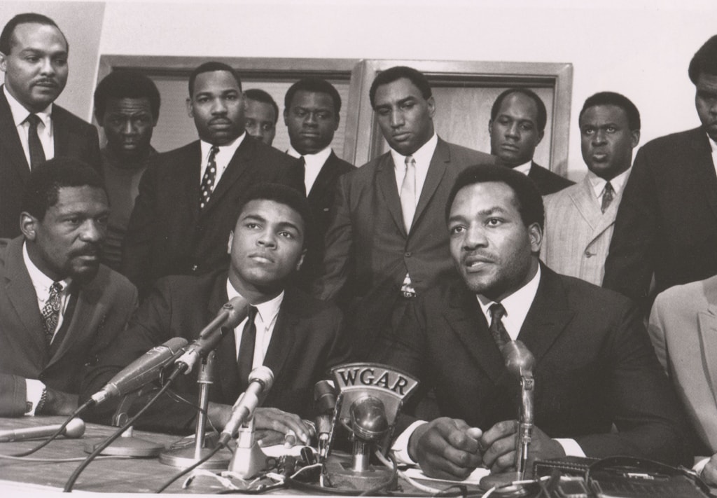 Black and white photo of Muhammad Ali at Cleveland Summit alongside Jim Brown and other athletes