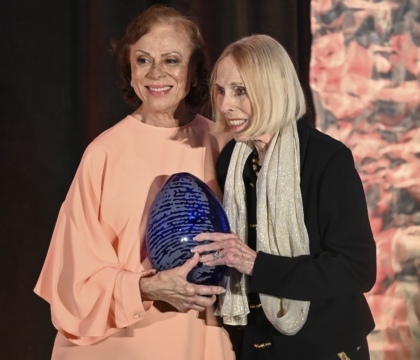 Two women posing for different camera while holding an award