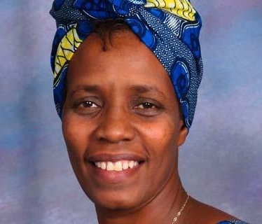 Woman wearing blue and yellow headwrap smiles at camera