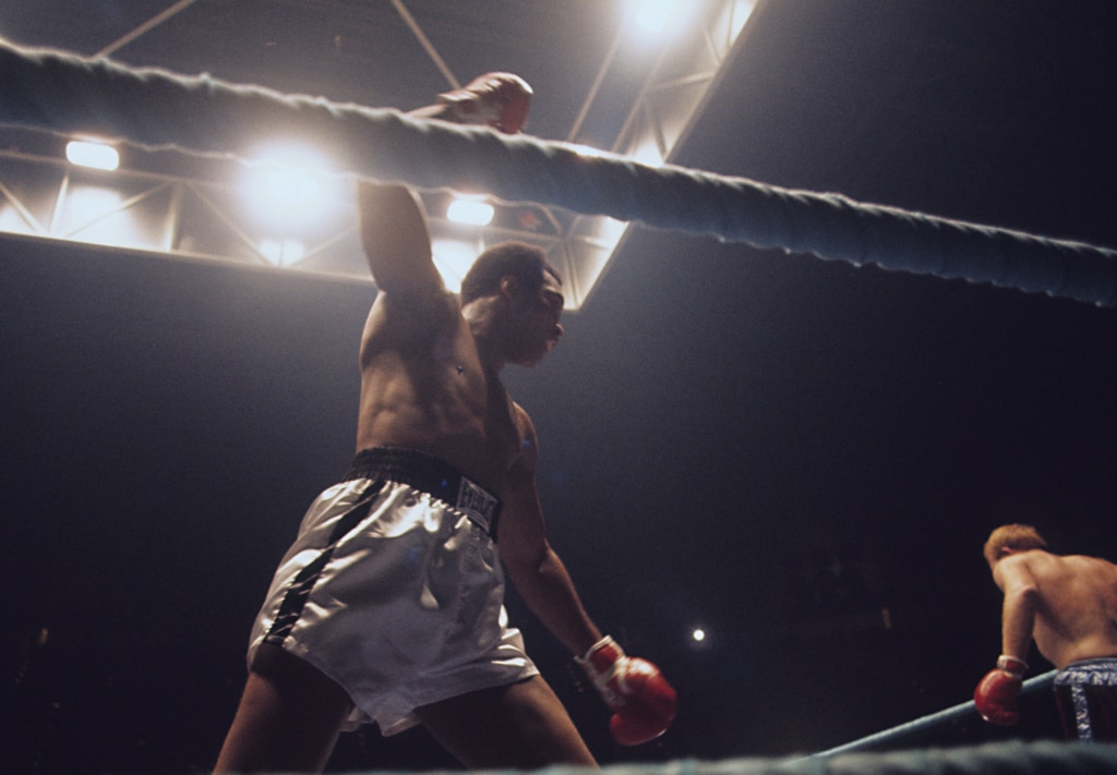 View of Muhammad from below as he raises gloved fist towards boxing opponent