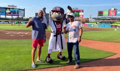 Two men pose with a bat mascot on a baseball field