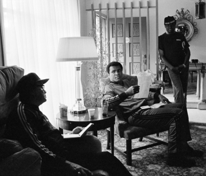 Black and white photo of Muhammad Ali sitting with friends inside a home