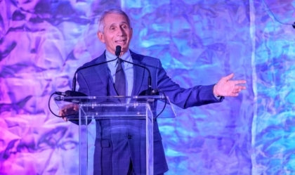 Dr. Fauci in a suit speaking at a lectern