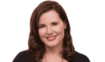 Geena Davis, wearing black top and gold necklace, smiles at camera