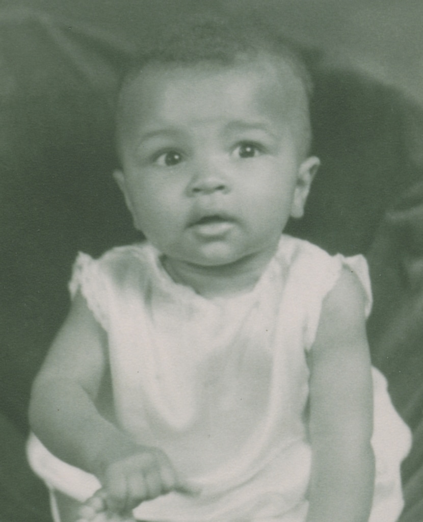 Black and white photo of baby Muhammad Ali (then Cassius Clay, Jr.) in white outfit