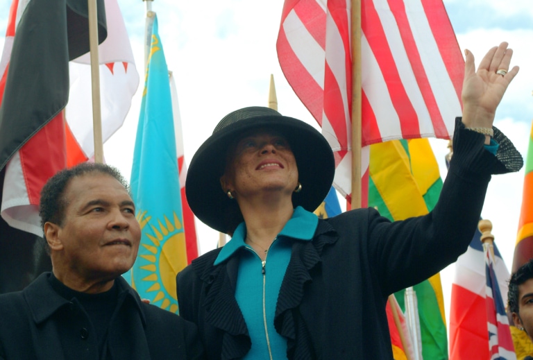 Photo of Lonnie Ali waving with Muhammad next to her and flags behind them