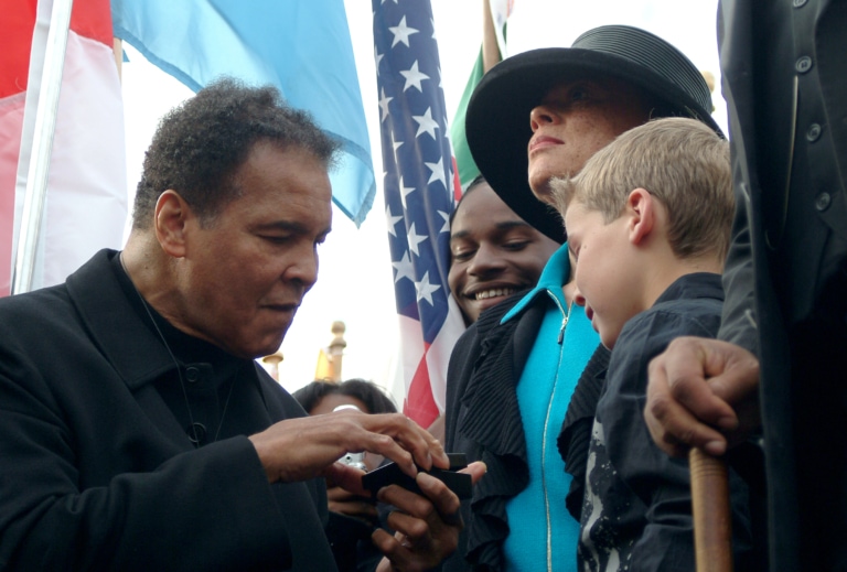 Photo of Muhammad Ali opening a box in front of children at celebration