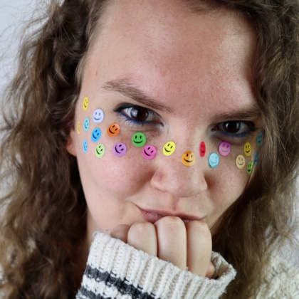 Woman wearing sweater looking at camera with smiley-face stickers on face