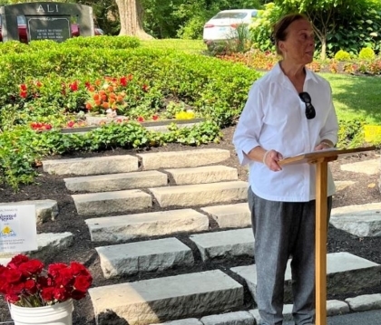 Lonnie Ali speaks at a podium in front of a grave with lots of flowers on it