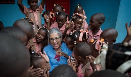 Woman wearing glasses and blue shirt smiles with group of children