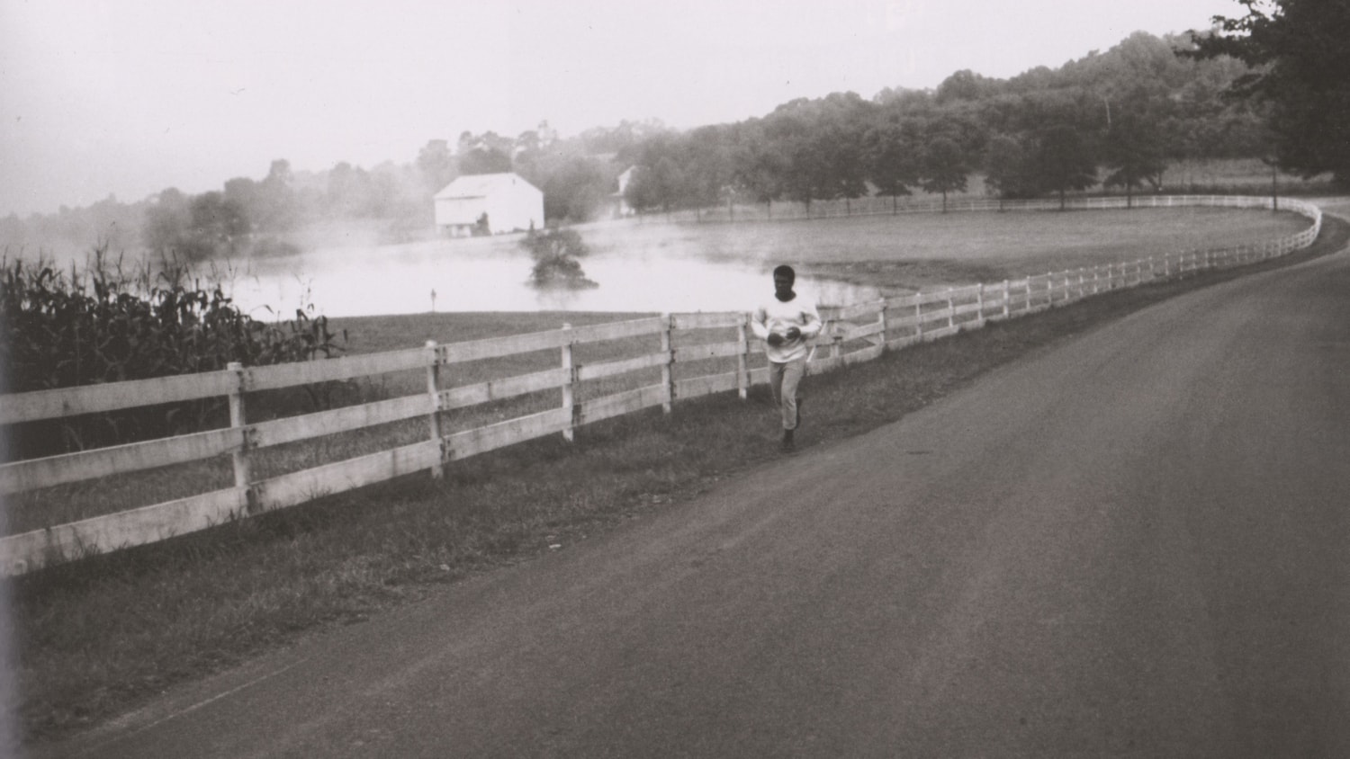 A man runs beside a fence on a long road