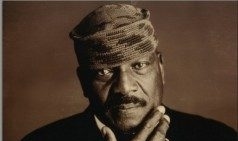 Jim Brown, wearing black jacket, white shirt and kufi hat poses with hand to his chin
