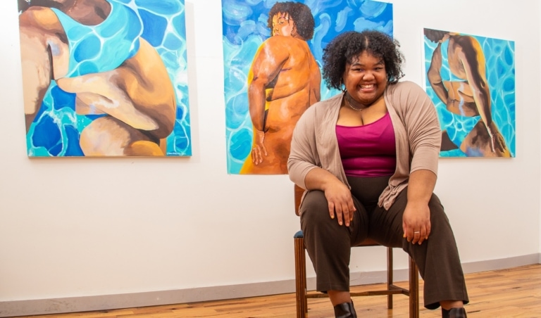 Woman sitting on chair in front of three paintings
