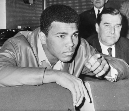 Black and white photo of Muhammad Ali in a jacket pointing