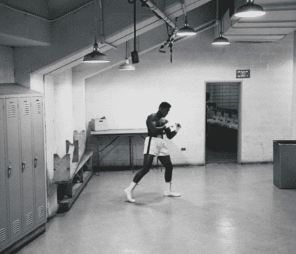 Black and white photo of Muhammad Ali in boxing gear in a locker room