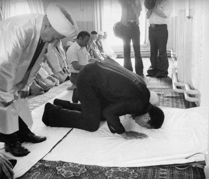 Black and white photo of Muhammad Ali praying with several other Muslim men
