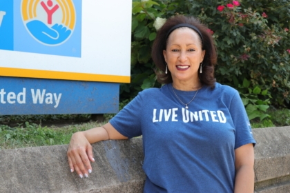 Woman standing in front of Metro United Way sign wearing a blue shirt with "Live United" text smiling at camera