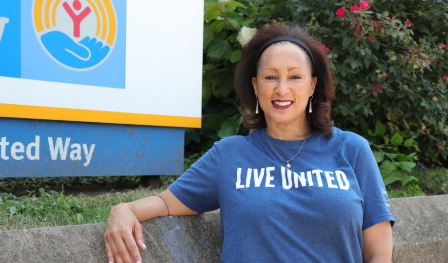 Woman standing in front of Metro United Way sign wearing a blue shirt with "Live United" text smiling at camera