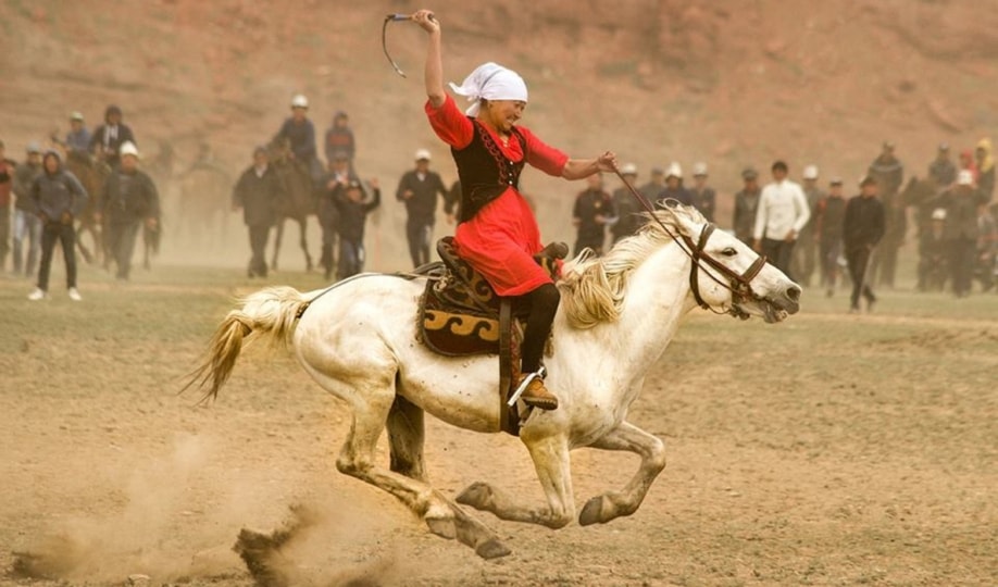 Photo of woman wearing red blouse, headscarf and black pants riding a white horse