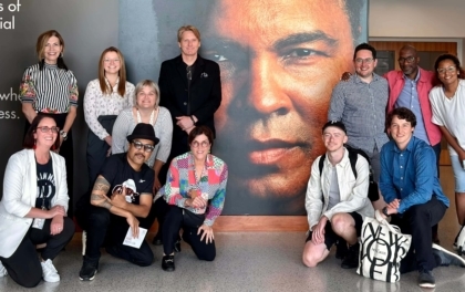 Group of people kneeling and standing in front of a large wall with a photo of Muhammad Ali's face