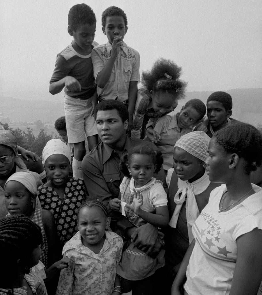 Black and white photo of Muhammad Ali outside with a large group of children