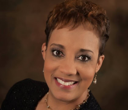 Photo of woman with short hair wearing black sweater and necklace looking up towards camera