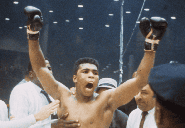 Photo of Muhammad Ali celebrating with gloves in the air