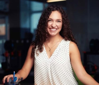 Photo of woman with curly brown hair wearing white spotted top smiling at camera